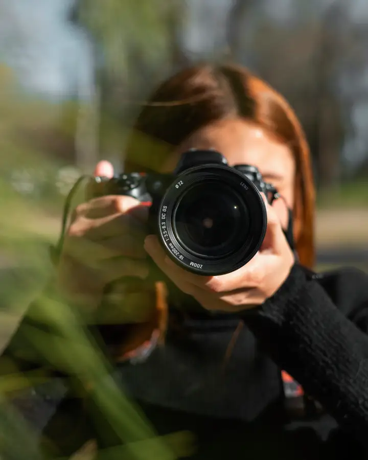 Photographer with camera in focus, capturing nature scenery outdoors on a sunny day.
